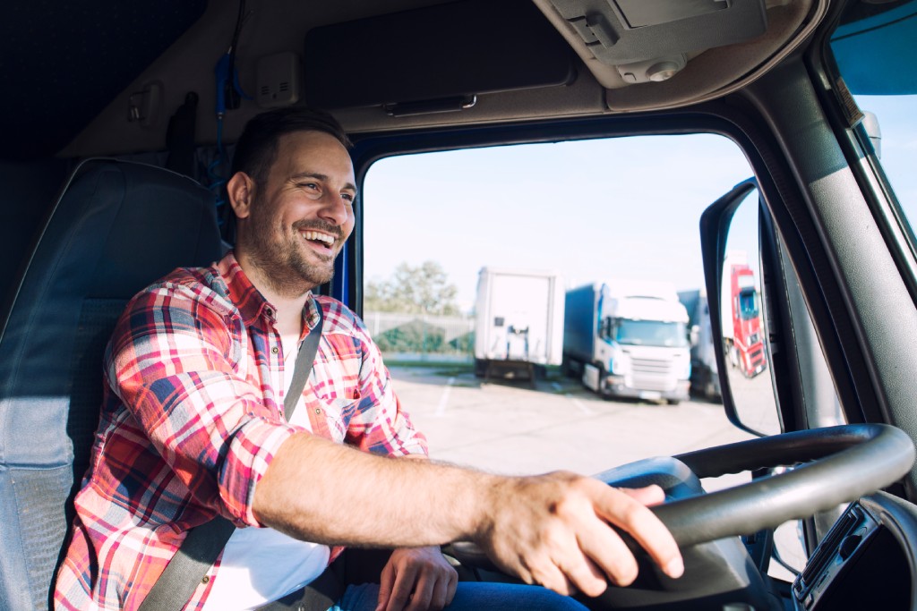 Truck driver job. Middle aged trucker driving truck. Professional middle aged truck driver in casual clothes driving truck vehicle and delivering cargo to destination.