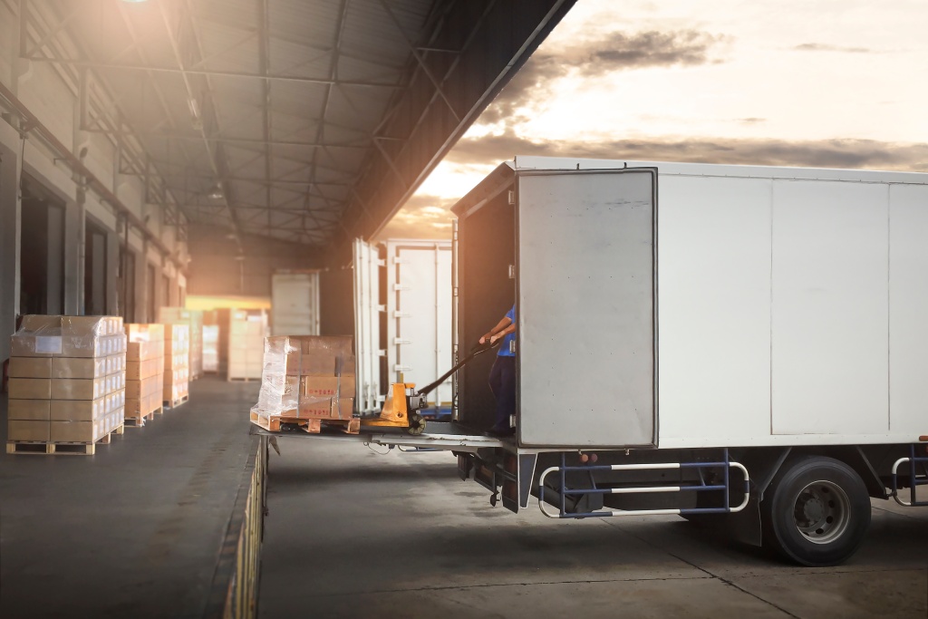 Worker Loading Package Boxes on Pallets into Cargo Container. Trucks Parked Loading at Dock Warehouse. Supply Chain Delivery Service. Shipping Warehouse Logistics. Road Freight Truck Transportation.