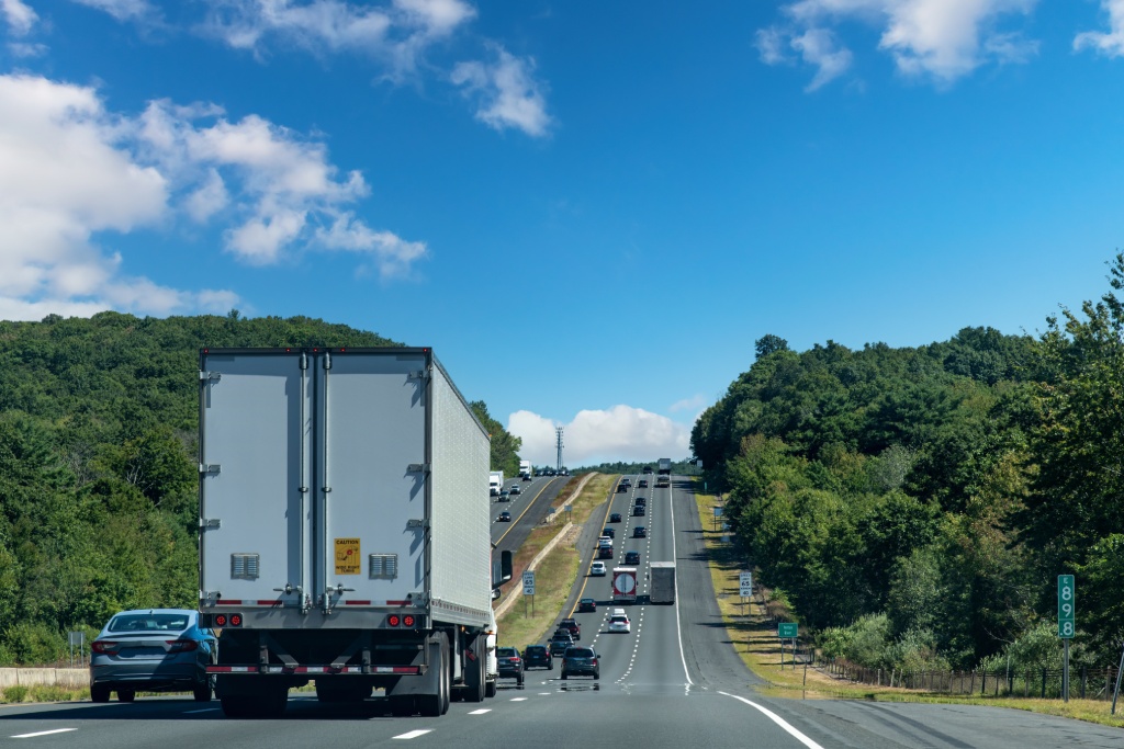 Drivers perspective view over busy and hilly Interstate 84 highway in northerly direction near Willington, CT, USA with trucks and cars on highway