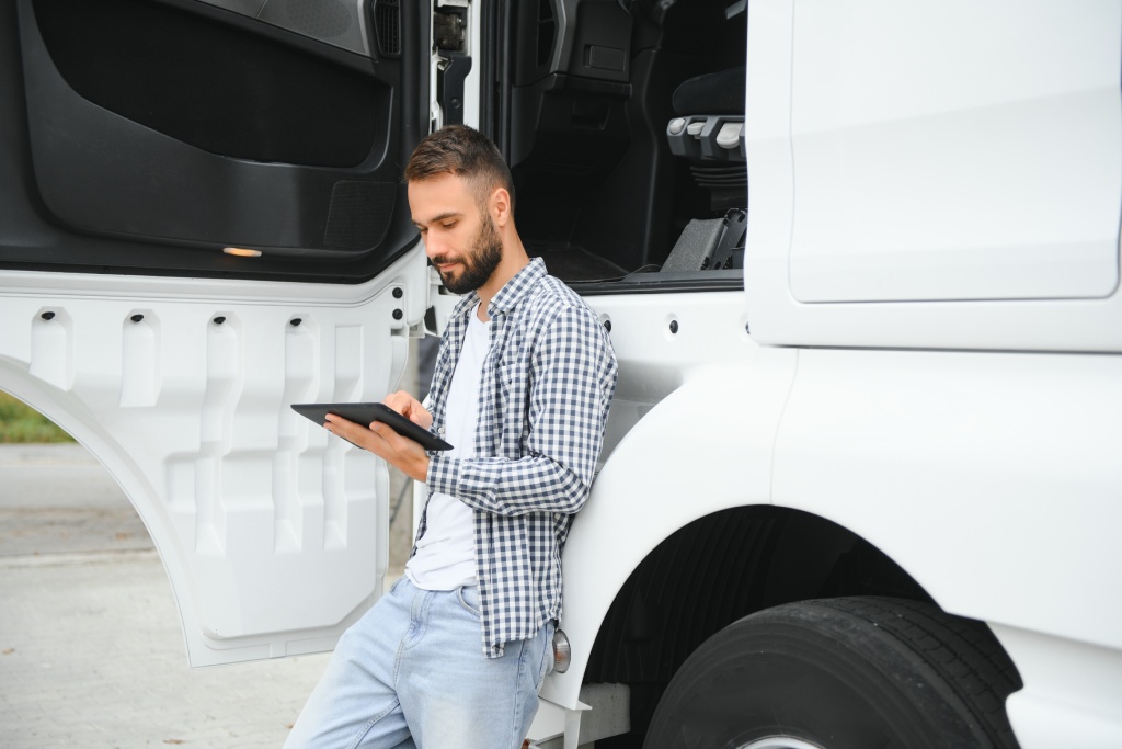 Young handsome truck driver is standing with a tablet near the truck.